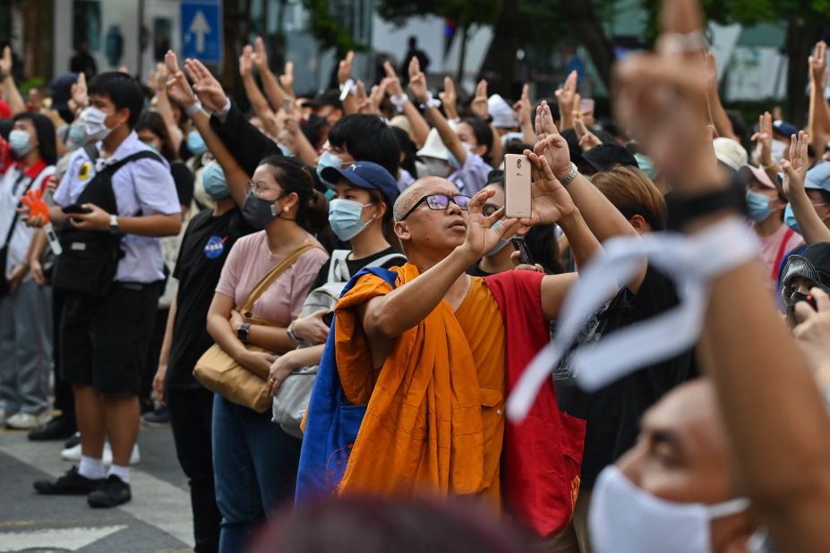 A monk takes photos with his mobile phone as protesters give the three-finger salute on October 15.