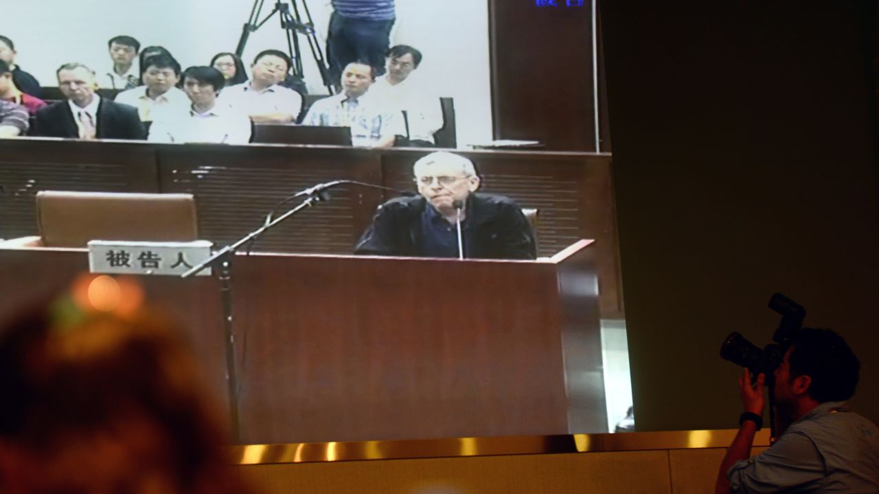 Journalists follow the progress on a television screen of the trial of British investigator Peter Humphrey (center) linked to beleaguered pharmaceutical giant GSK and his wife, at the Shanghai Intermediate Court on August 8, 2014.