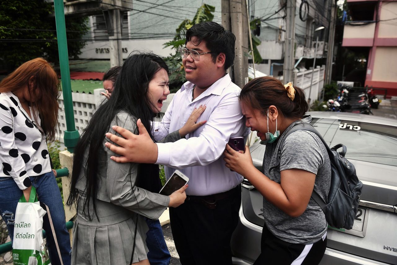 Pro-democracy activist Bunkueanun "Francis" Paothong, center, comforts loved ones before he enters the Dusit Police Station on October 16, to answer charges of harming Thailand's Queen Suthida, two days after protesters nearly obstructed a royal motorcade.