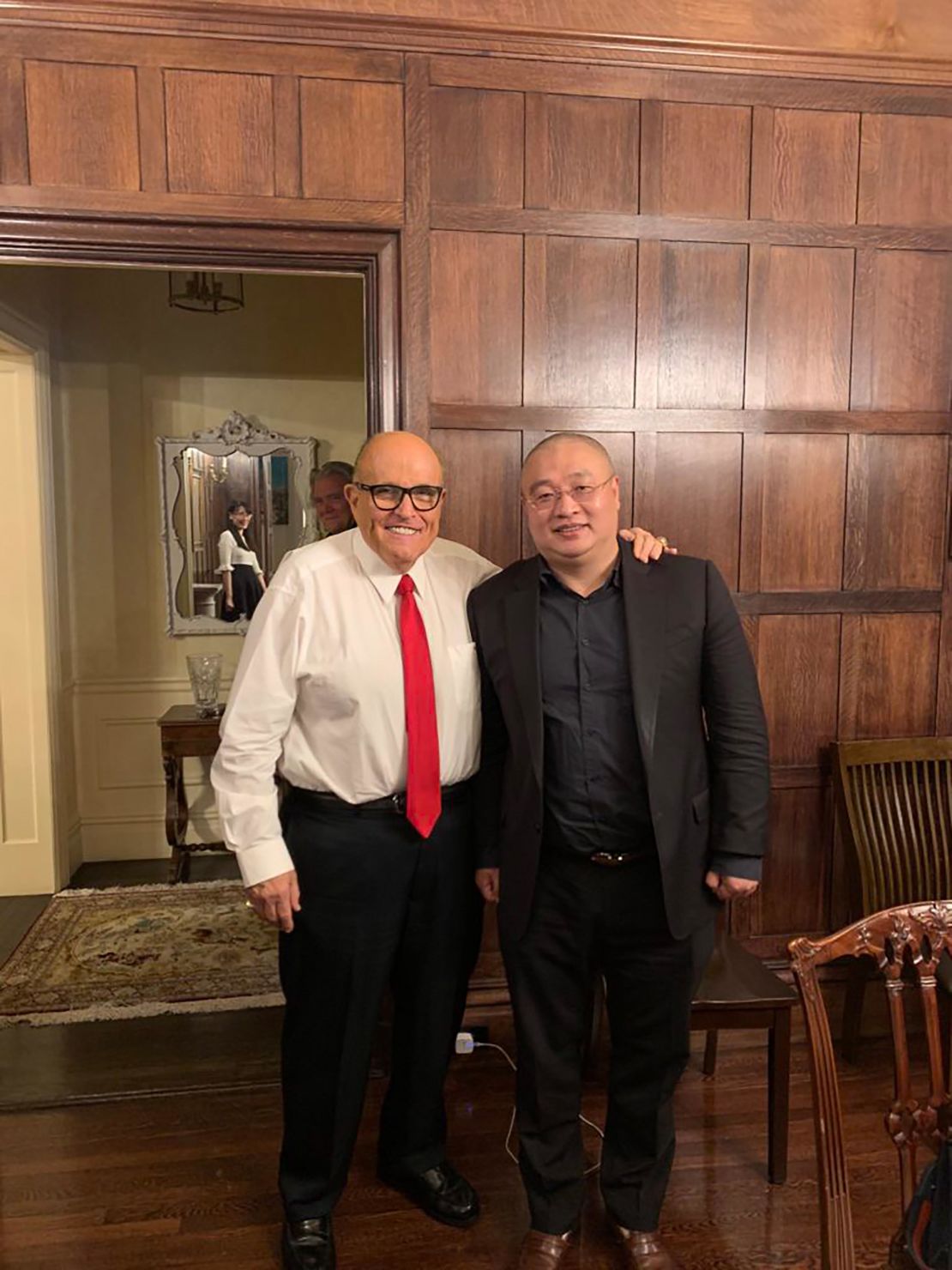 This photo appears to capture the reflection of virologist Li-Meng Yan in the mirror behind the two men in the foreground: Wang DingGang, board chair of the Rule of Law Society, and former New York City Mayor Rudy Giuliani. Bannon's image can also be seen in the photo.