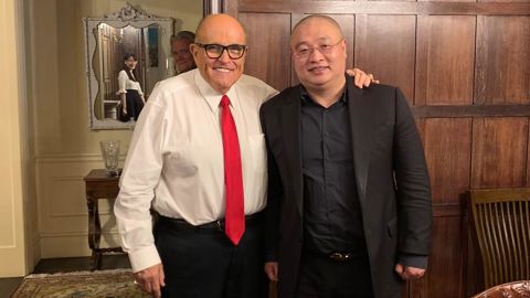 This photo appears to capture the reflection of virologist Li-Meng Yan in the mirror behind the two men in the foreground: Wang DingGang, board chair of the Rule of Law Society, and former New York City Mayor Rudy Giuliani. Bannon's image can also be seen in the photo.