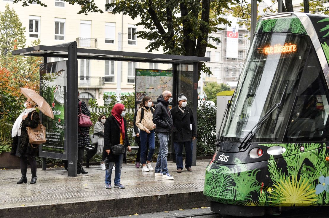 People wearing protective face masks wait for a tram on October 22, 2020 in a street of Saint-Etienne, central eastern France.