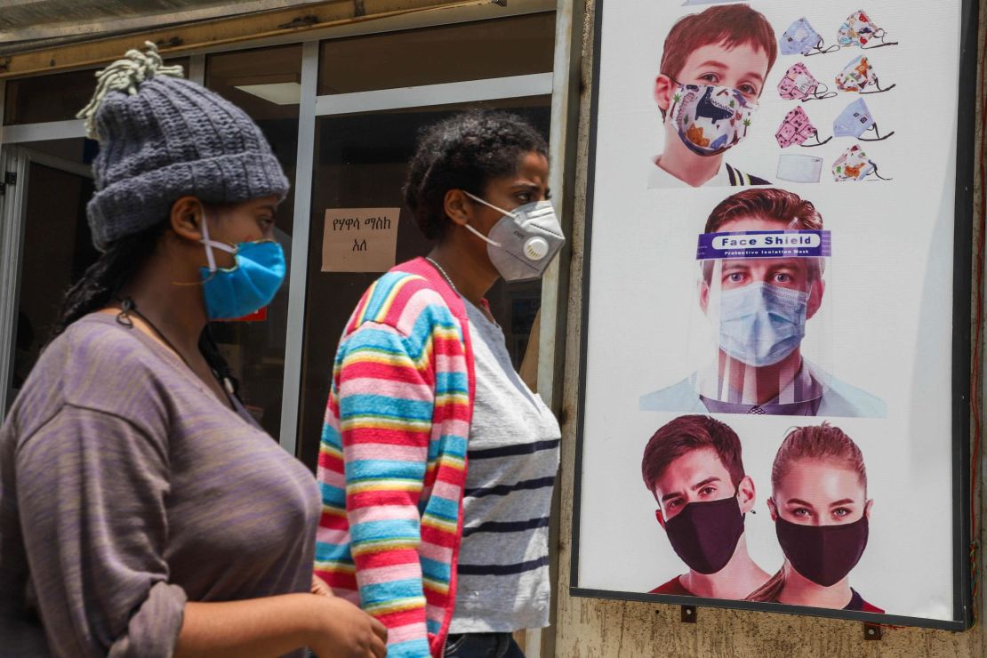 People wearing face masks walk past a poster promoting the use of face mask and face shield in Addis Ababa on August 21.