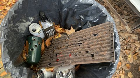 Cans, an empty bottle of whisky, and items with apparent bullet holes in a trash bin near Garbin's mobile home.