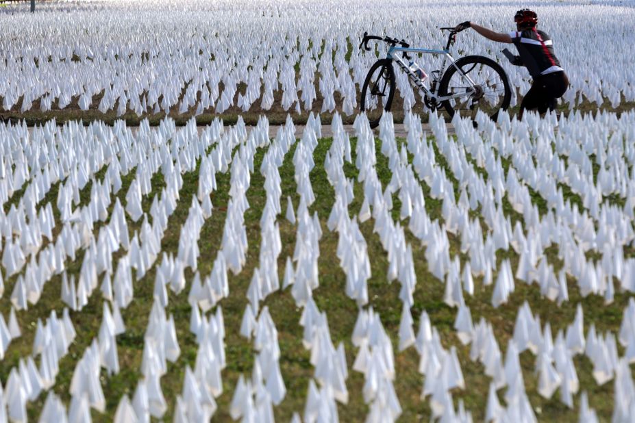 A cyclist takes pictures of a public art project set up on the DC Armory Parade Ground in Washington, DC. An estimated 240,000 flags were planted to represent lives lost to Covid-19. The display, created by local artist Susanne Brennan Firstenberg, was on display for two weeks.