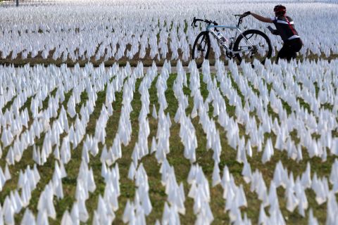 A cyclist takes pictures of a public art project set up on the DC Armory Parade Ground in Washington, DC. An estimated 240,000 flags were planted to represent lives lost to Covid-19. The display, created by local artist Susanne Brennan Firstenberg, was on display for two weeks.