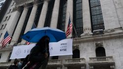 A woman with an umbrella passes the New York Stock Exchange, Monday, Oct. 26, 2020. Stocks are slumping in afternoon trading on Wall Street Monday and deepening last week's losses. (AP Photo/Mark Lennihan)