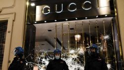 Italian police officers stand in front of a shattered Gucci store window during a protest of far-right activists against the government restriction measures to curb the spread of COVID-19, in downtown Turin, on October 26, 2020, as the country faces a second wave of infections to the Covid-19 (the novel coronavirus). - Italy's Prime Minister Giuseppe Conte tightened nationwide coronavirus restrictions on October 25, 2020 after the country registered a record number of new cases, despite opposition from regional heads and street protests over curfews. Cinemas, theatres, gyms and swimming pools must all close under the new rules, which come into force on October 26, 2020 and run until November 24, while restaurants and bars will stop serving at 6pm, the prime minister's office said. (Photo by Marco BERTORELLO / AFP) (Photo by MARCO BERTORELLO/AFP via Getty Images)