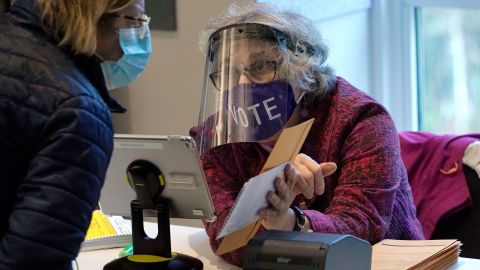 A well-protected poll worker in Newton, Mass., cuts down on the risk of voting. Do your part by wearing a mask and social distancing.