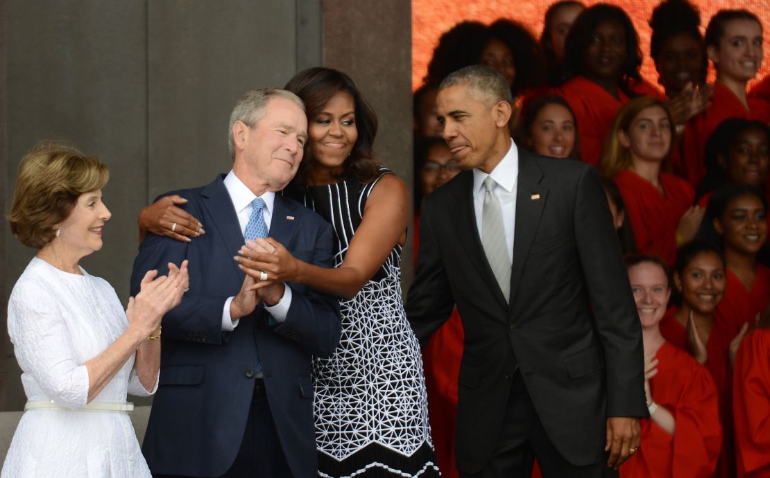 President Barack Obama watches first lady Michelle Obama embracing former president George W. Bush, accompanied by his wife, former first lady Laura Bush, at the dedication of the National Museum of African American History and Culture September 24, 2016 in Washington, DC.