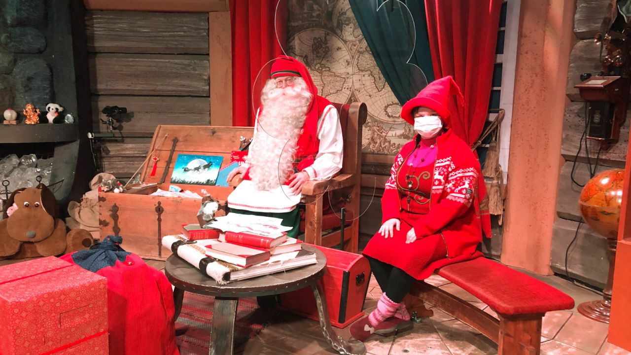 Santa sits behind plexiglass while his elves wear masks in Lapland.
