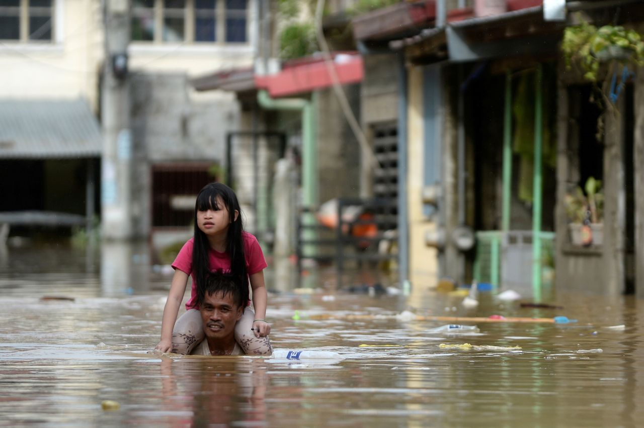 A man carries a child on his shoulders as he wades through a flooded street in the Rizal province.