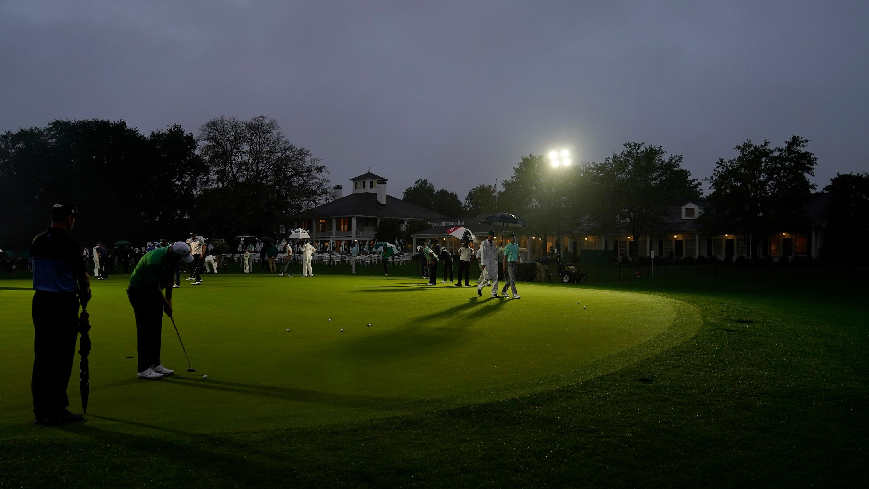 Golfers practice on the putting green next near the Augusta National Golf Course clubhouse before the start of the first round in near darkness.