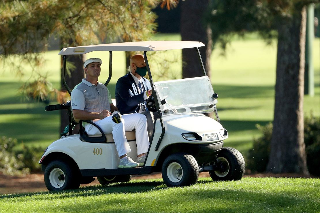 Bryson DeChambeau rides in a cart with a rules official after playing his second tee shot on the third hole where he ran up a disastrous triple bogey.