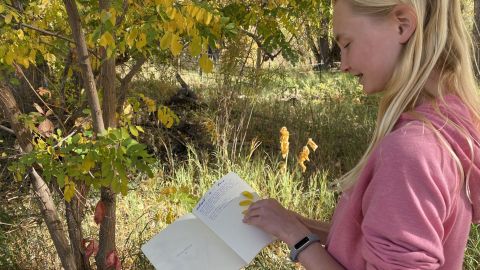 A student works on her nature journal, describing a yellow leaf from a tree she adopted. 