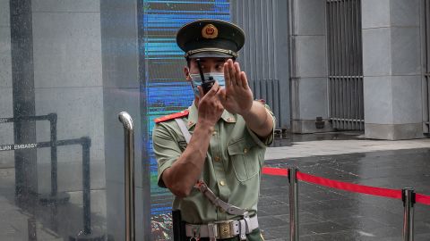 A Chinese paramilitary police officer gestures and speaks over his two-way radio whlie standing at the entrance gate of the Australian embassy in Beijing on July 9, 2020.