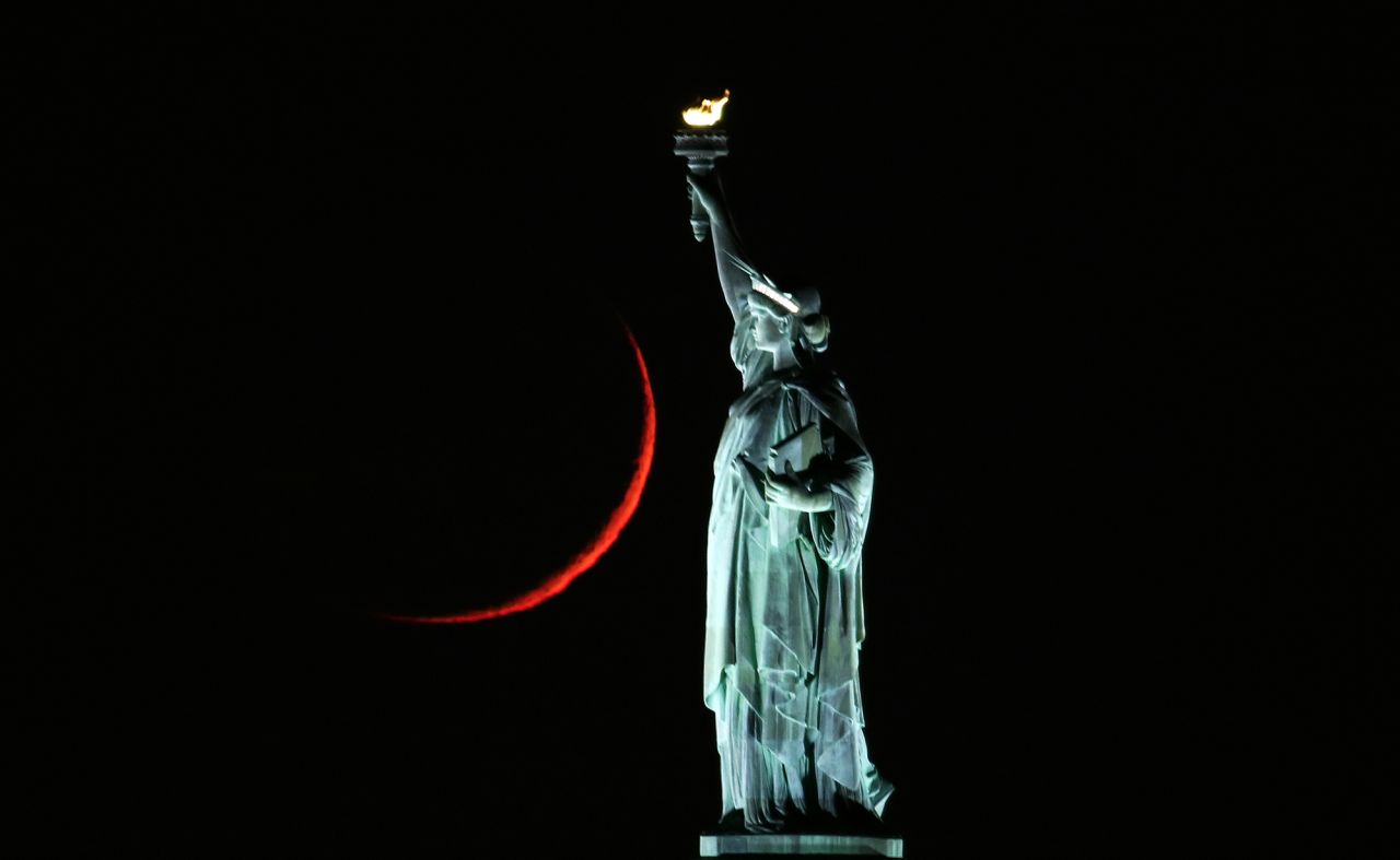 The moon sets behind the Statue of Liberty on Monday, November 16, in New York.