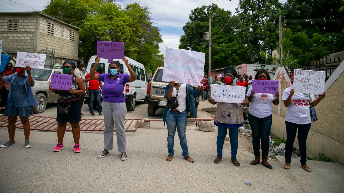 Women hold up signs demanding justice during the hearing of president of the Haitian Football Federation Jean-Bart.