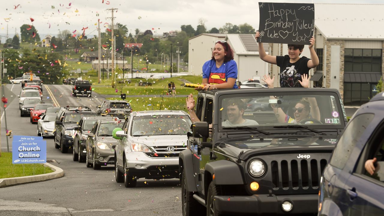People hold birthday signs and shoot confetti during a drive-by birthday parade for 8-year-old Riley Rejniak in Leesport, Pennsylvania.