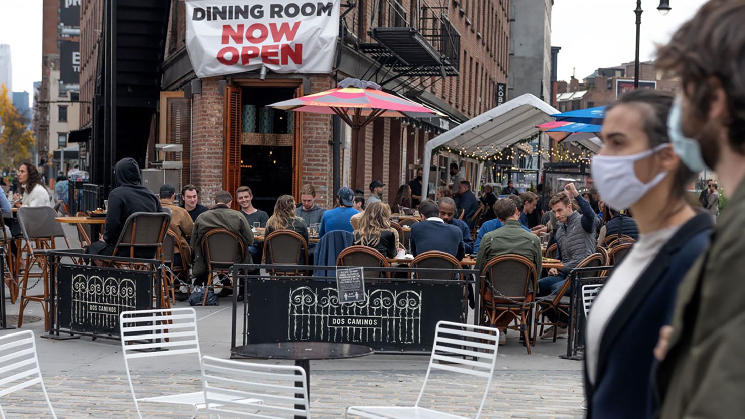 People wearing masks walk by people dining in New York City.