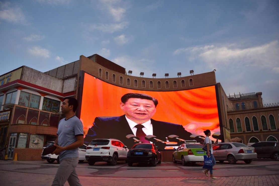 This photo taken on June 4, 2019, at the end of Ramadan, shows people walking past a screen showing images of Chinese President Xi Jinping in Kashgar, in China's western Xinjiang region. 