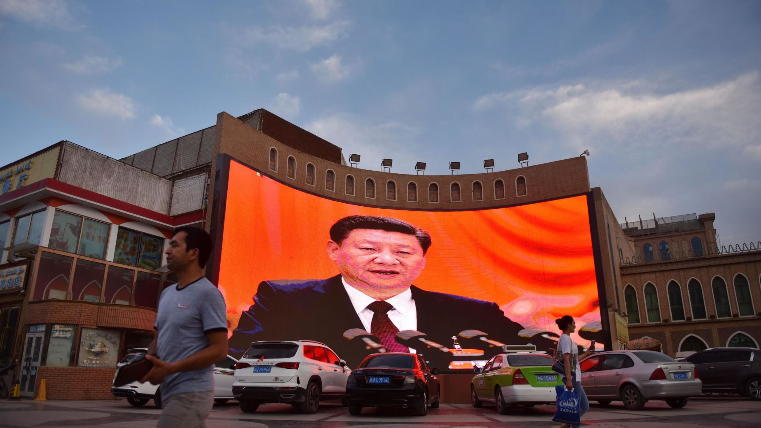 This photo taken on June 4, 2019 shows people walking past a screen displaying images of Chinese President Xi Jinping in Kashgar, western Xinjiang.