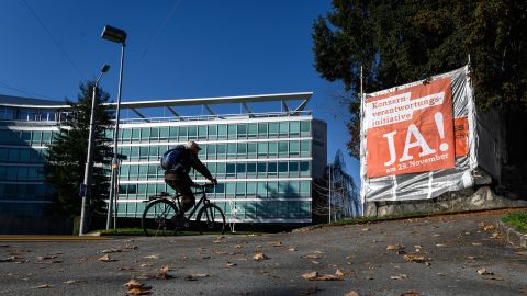 A man rides his bicycle next to the headquarters of Swiss food giant Nestlé and a campaign banner encouraging citizens to vote in favor of the Responsible Business Initiative.