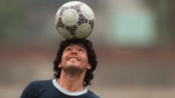 Argentine soccer star Diego Maradona, wearing a diamond earring, balances a soccer ball on his head as he walks off the practice field following the national selection's 22 May 1986 practice session in Mexico City. (Photo credit should read JORGE DURAN/AFP via Getty Images)