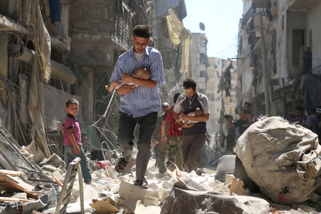 Syrian men carrying babies make their way through the rubble of destroyed buildings following an air strike in Aleppo on September 11, 2016.