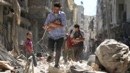 Syrian men carrying babies make their way through the rubble of destroyed buildings following a reported air strike on the rebel-held Salihin neighborhood of the northern city of Aleppo, on September 11, 2016.
