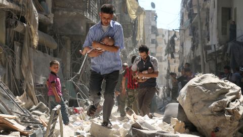 Syrian men carrying babies make their way through the rubble of destroyed buildings following an air strike in Aleppo on September 11, 2016.