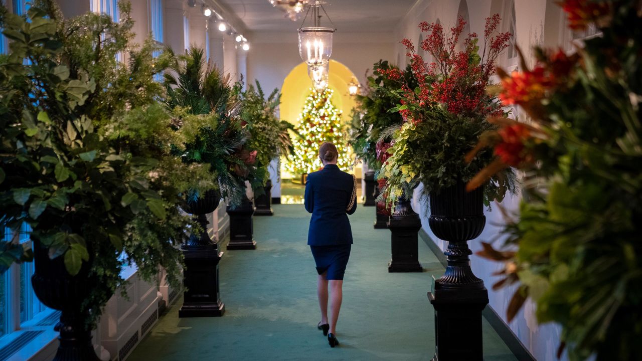 A military aide walks between Christmas decorations in the East Wing of the White House on Monday.