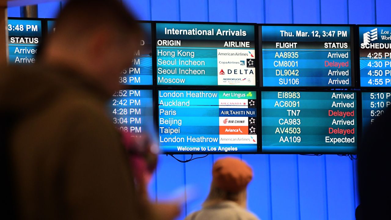 International flights arrivals are listed on a screen at Los Angeles International Airport on March 12, 2020 one day before a US flight travel ban hits 26 European countries amid ongoing precautions over the Coronavirus. 