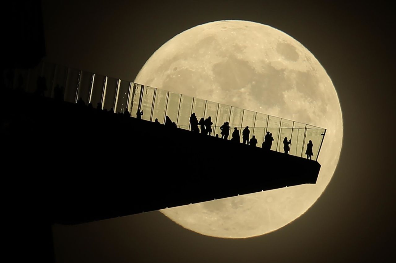 A full moon is seen behind people standing on the Edge, an outdoor observation deck in New York City, on Sunday, November 29.