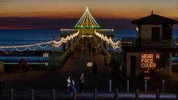 MANHATTAN BEACH, CA - DECEMBER 03: With annual holiday decorations on display, a city sign alerts visitors to the Pier in Manhattan Beach, CA, that face coverings are required, or face up to a $350 fine, on Thursday, Dec. 3, 2020. Due to increases in COVID-19 cases across Southern California, the city of Manhattan Beach is requiring anyone out in public to wear a face covering, or face fines. (Jay L. Clendenin / Los Angeles Times via Getty Images)