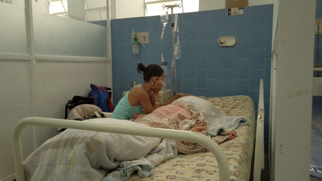 A woman pictured in Vargas Hospital in Caracas, Venezuela with her 69-year-old father, who she told CNN is suffering from malnourishment and sharing a ward with a Covid-19 patient despite his compromised immune system.