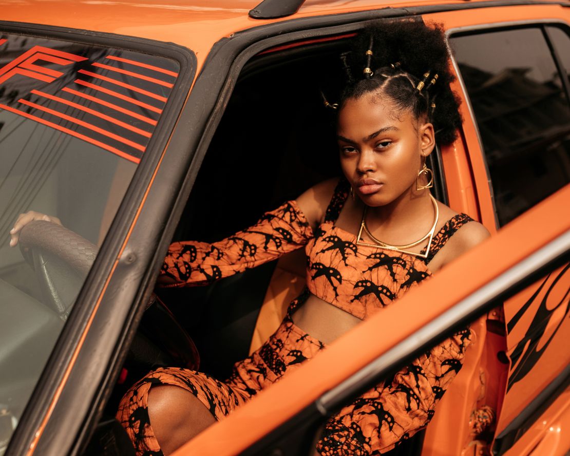 Christel Kattenstroth poses with her finished hairstyle inside an orange car with a matching outfit.