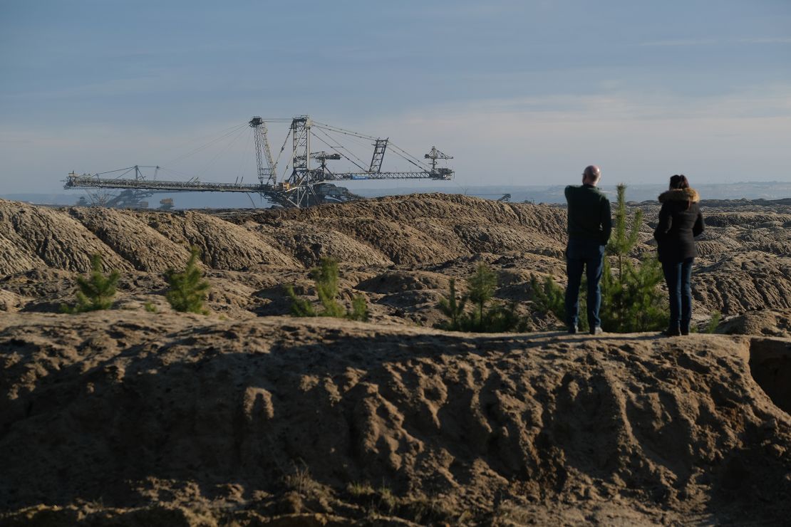 Visitors look at a giant machine called a spreader dumping earth near an open-pit coal mine in Neupetershain, Germany. As people have dramatically cut into the natural world, they have also ramped up the production of materials in the last 120 years, a new study finds.
