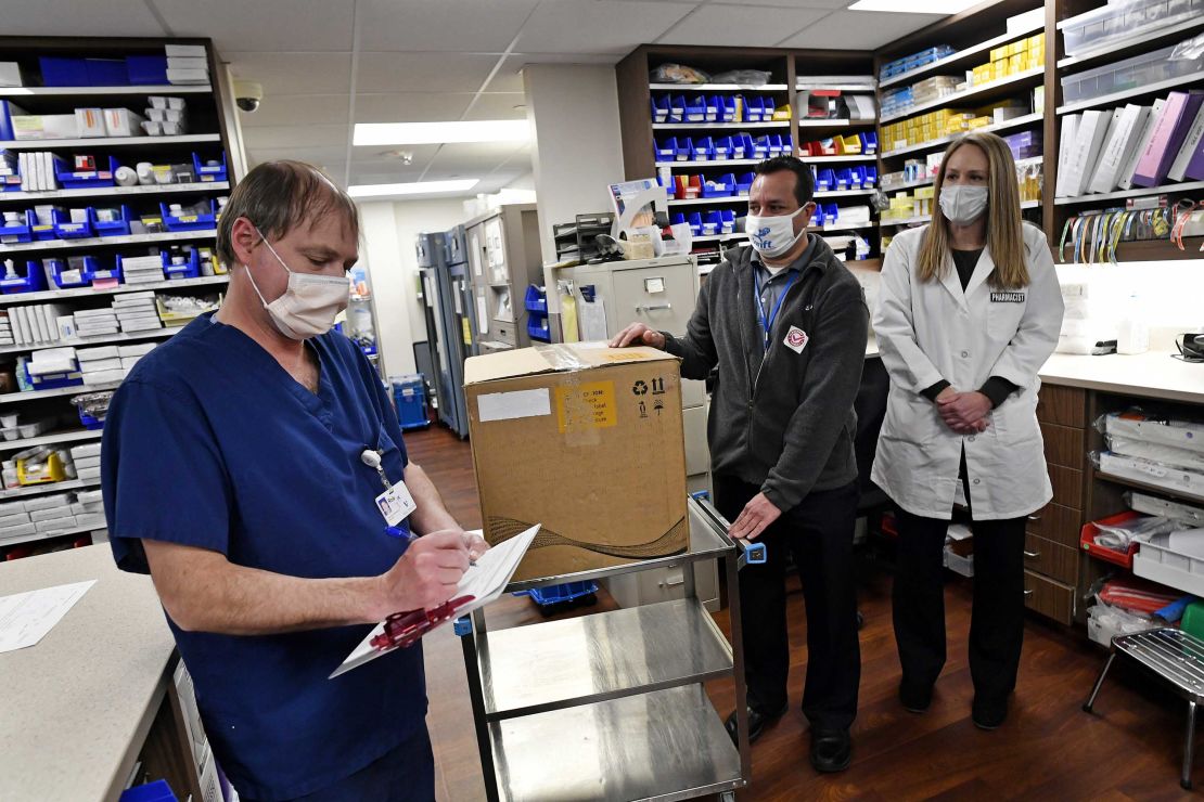 Vail Health Hospital pharmacy technician Rob Brown, left, signs the necessary paperwork to take possession of mock Covid-19 vaccines from courier driver Leo Gomez, center, as pharmacist Jessica Peterson watches over the process in the pharmacy on December 8, 2020, in Vail, Colorado.  