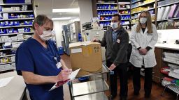 Vail Health Hospital pharmacy technician Rob Brown, left, signs the necessary paperwork to take possession of mock Covid-19 vaccines from courier driver Leo Gomez, center, as pharmacist Jessica Peterson watches over the process in the pharmacy on December 8, 2020 in Vail, Colorado.  With the state expecting its first shipment of a COVID-19 vaccine in a matter of days, the state health department ran an exercise to see how ready it is to take on such a mass vaccination campaign. The Pfizer vaccine, which is the first shot expected to gain federal approval, will be difficult for the state to distribute as it needs to be stored at sub-zero temperatures and requires two shots. The Colorado Division of Homeland Security and Emergency Management held a dry run or drill of receiving the vaccines in a thermal shipping container at Denver International Airport, using a courier car to take the vaccines to Vail Health Hospital and then the path the vaccines will follow once at the hospital from the pharmacy to a patient receiving the vaccine. (Photo by Helen H. Richardson/MediaNews Group/The Denver Post via Getty Images)
