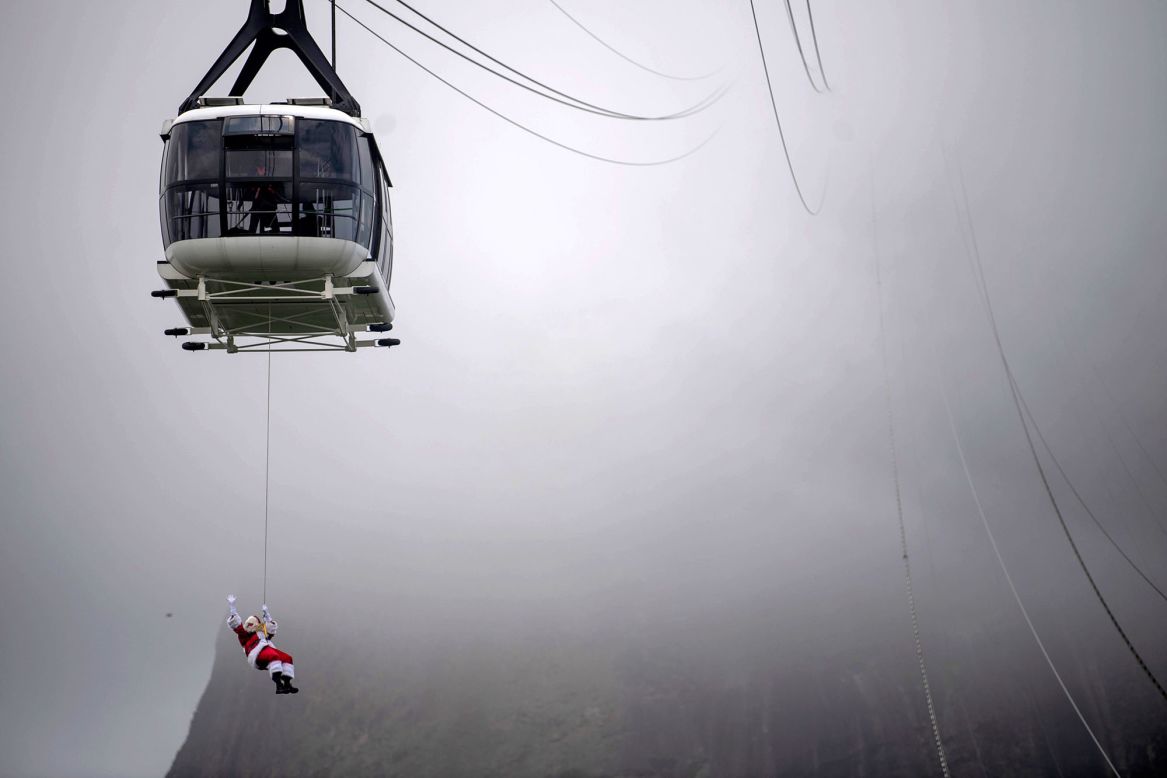 A man in a Santa Claus costume, suspended from a cable car, waves at visitors arriving to Rio de Janeiro's Sugarloaf Mountain on Saturday, December 5.