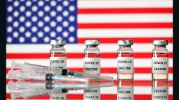 An illustration picture shows vials with Covid-19 Vaccine stickers attached, and syringes, with a flag of the United States, on November 17, 2020. (Photo by JUSTIN TALLIS / AFP) (Photo by JUSTIN TALLIS/AFP via Getty Images)