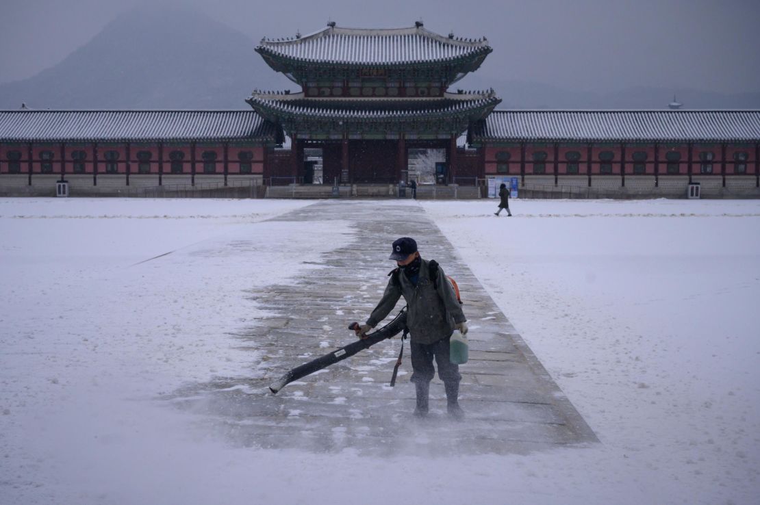 A worker uses a blower to clear snow from a courtyard at Gyeongbokgung Palace in central Seoul on December 13, 2020.