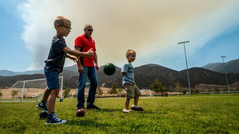 Temescal Canyon resident Gregory Tucker (center), plays bocce ball with grandsons Mason (left), 5, and Griffin (right), 4, at Deleo Regional Sports Park as a smoke plume from the Holy fire blankets the sky near Corona, California, August 7, 2018.