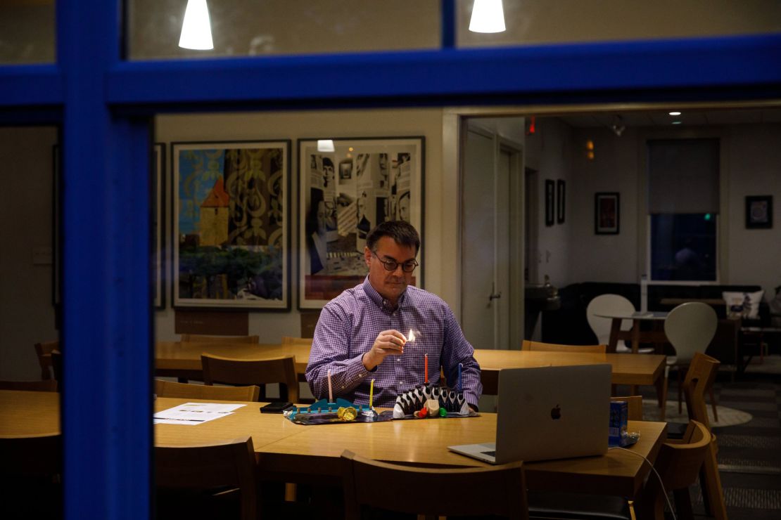 Through the window of Rothenberg Hillel House at Kenyon College in Ohio, Jewish Chaplain Marc Bragin can be seen lighting a candle over Zoom to mark the first night of Hanukkah.