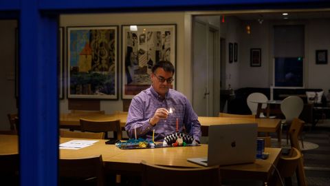Through the window of Rothenberg Hillel House at Kenyon College in Ohio, Jewish Chaplain Marc Bragin can be seen lighting a candle over Zoom to mark the first night of Hanukkah.
