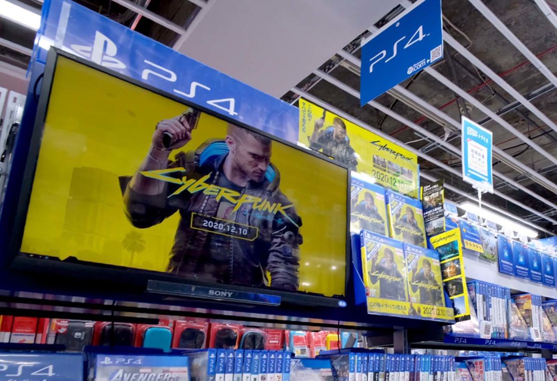 A screen shows a promotional video for "Cyberpunk 2077" in a store in Tokyo. Physical copies are still being sold.