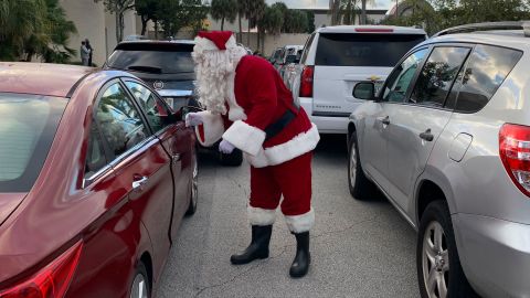 Santa spreads cheer to people waiting in line for food. Cadillacs and other expensive cars were in the line.