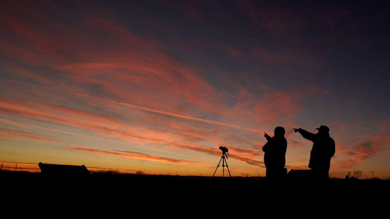 People are silhouetted against the sky at dusk as they watch the alignment Monday in Edgerton, Kansas. 