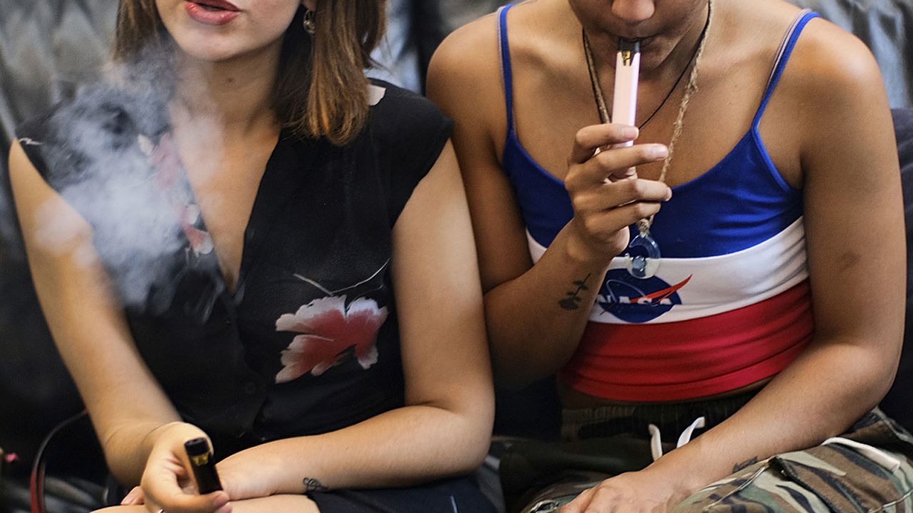 In June 2019, two women smoke cannabis vape pens at a party in Los Angeles. A national outbreak of deadly lung illnesses tied to vaping transpired that year. 